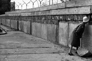 Black and white historical photograph of a woman standing at the Berlin Wall circa 1962 for Flash Fiction: Cold War by Malin James